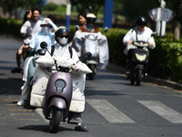 Citizens are wearing sun-protective clothing and riding on a street under high temperatures in Fuyang, China, on June 14, 2024. (