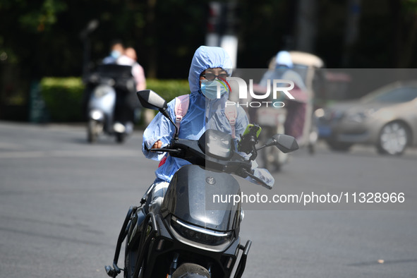 Citizens are wearing sun-protective clothing and riding on a street under high temperatures in Fuyang, China, on June 14, 2024. 