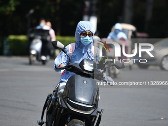 Citizens are wearing sun-protective clothing and riding on a street under high temperatures in Fuyang, China, on June 14, 2024. (