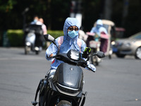 Citizens are wearing sun-protective clothing and riding on a street under high temperatures in Fuyang, China, on June 14, 2024. (