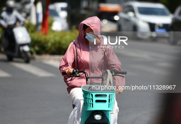 Citizens are wearing sun-protective clothing and riding on a street under high temperatures in Fuyang, China, on June 14, 2024. 