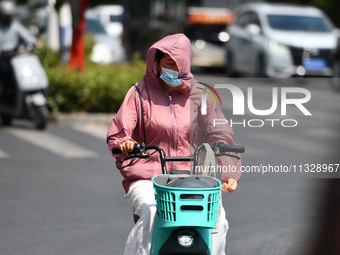 Citizens are wearing sun-protective clothing and riding on a street under high temperatures in Fuyang, China, on June 14, 2024. (