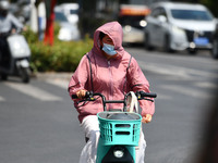 Citizens are wearing sun-protective clothing and riding on a street under high temperatures in Fuyang, China, on June 14, 2024. (