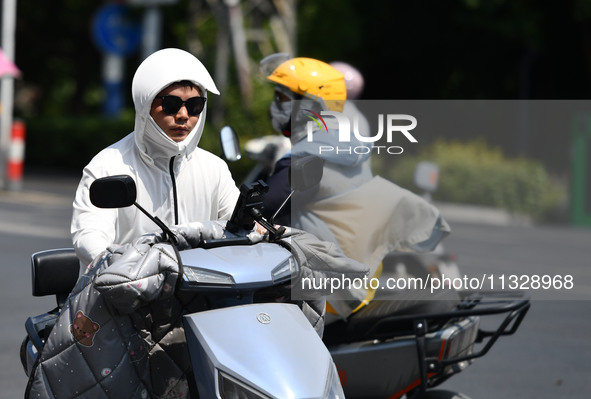 Citizens are wearing sun-protective clothing and riding on a street under high temperatures in Fuyang, China, on June 14, 2024. 