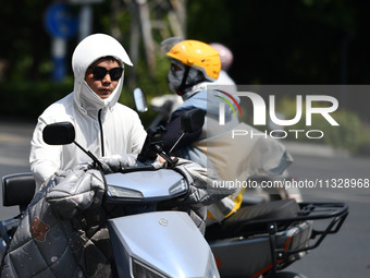 Citizens are wearing sun-protective clothing and riding on a street under high temperatures in Fuyang, China, on June 14, 2024. (