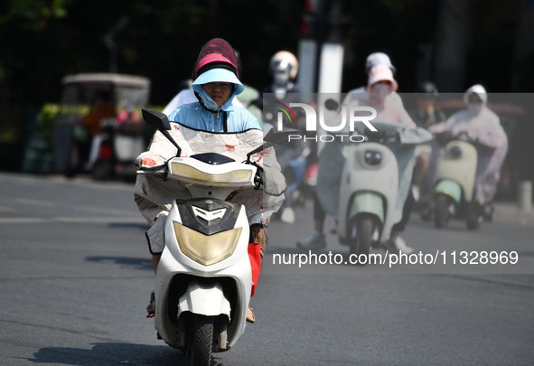 Citizens are wearing sun-protective clothing and riding on a street under high temperatures in Fuyang, China, on June 14, 2024. 