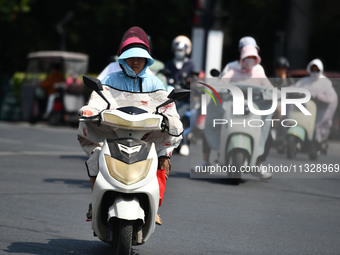 Citizens are wearing sun-protective clothing and riding on a street under high temperatures in Fuyang, China, on June 14, 2024. (