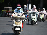 Citizens are wearing sun-protective clothing and riding on a street under high temperatures in Fuyang, China, on June 14, 2024. (