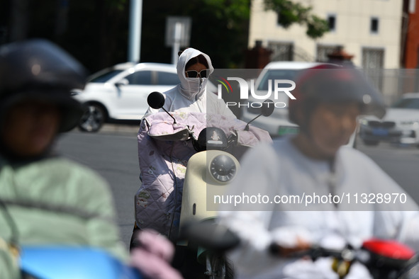 Citizens are wearing sun-protective clothing and riding on a street under high temperatures in Fuyang, China, on June 14, 2024. 