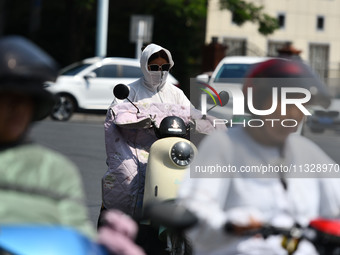 Citizens are wearing sun-protective clothing and riding on a street under high temperatures in Fuyang, China, on June 14, 2024. (