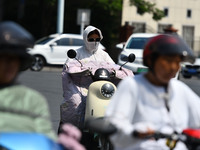 Citizens are wearing sun-protective clothing and riding on a street under high temperatures in Fuyang, China, on June 14, 2024. (