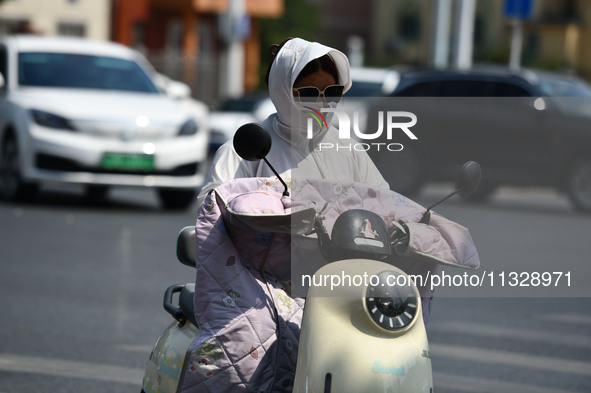 Citizens are wearing sun-protective clothing and riding on a street under high temperatures in Fuyang, China, on June 14, 2024. 