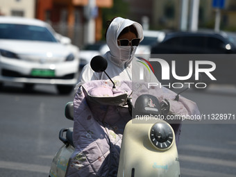 Citizens are wearing sun-protective clothing and riding on a street under high temperatures in Fuyang, China, on June 14, 2024. (