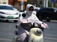 Citizens are wearing sun-protective clothing and riding on a street under high temperatures in Fuyang, China, on June 14, 2024. (