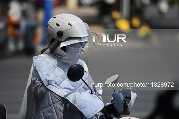 Citizens are wearing sun-protective clothing and riding on a street under high temperatures in Fuyang, China, on June 14, 2024. 