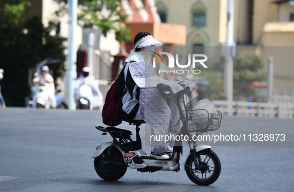 Citizens are wearing sun-protective clothing and riding on a street under high temperatures in Fuyang, China, on June 14, 2024. 