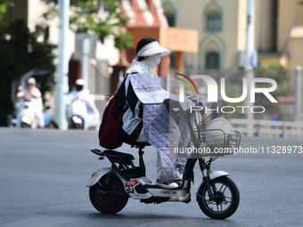 Citizens are wearing sun-protective clothing and riding on a street under high temperatures in Fuyang, China, on June 14, 2024. (