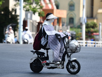 Citizens are wearing sun-protective clothing and riding on a street under high temperatures in Fuyang, China, on June 14, 2024. (