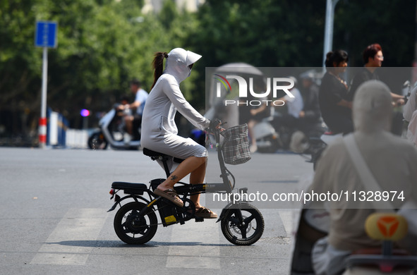 Citizens are wearing sun-protective clothing and riding on a street under high temperatures in Fuyang, China, on June 14, 2024. 