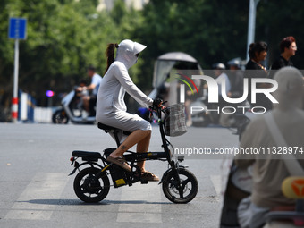 Citizens are wearing sun-protective clothing and riding on a street under high temperatures in Fuyang, China, on June 14, 2024. (