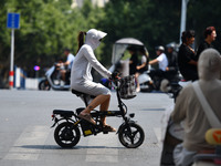 Citizens are wearing sun-protective clothing and riding on a street under high temperatures in Fuyang, China, on June 14, 2024. (