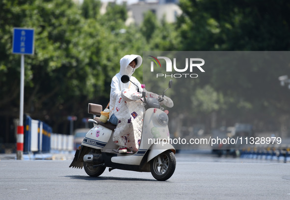 Citizens are wearing sun-protective clothing and riding on a street under high temperatures in Fuyang, China, on June 14, 2024. 