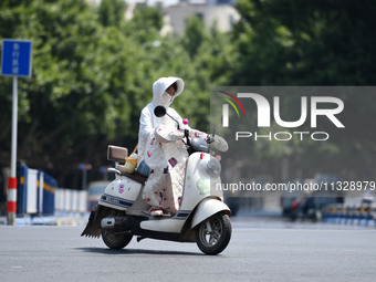 Citizens are wearing sun-protective clothing and riding on a street under high temperatures in Fuyang, China, on June 14, 2024. (