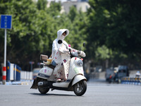 Citizens are wearing sun-protective clothing and riding on a street under high temperatures in Fuyang, China, on June 14, 2024. (