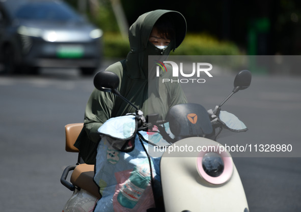 Citizens are wearing sun-protective clothing and riding on a street under high temperatures in Fuyang, China, on June 14, 2024. 