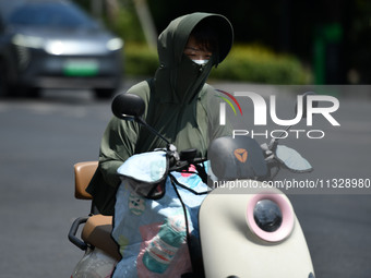 Citizens are wearing sun-protective clothing and riding on a street under high temperatures in Fuyang, China, on June 14, 2024. (