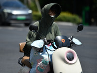 Citizens are wearing sun-protective clothing and riding on a street under high temperatures in Fuyang, China, on June 14, 2024. (