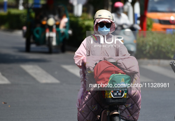 Citizens are wearing sun-protective clothing and riding on a street under high temperatures in Fuyang, China, on June 14, 2024. 