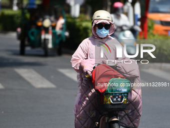 Citizens are wearing sun-protective clothing and riding on a street under high temperatures in Fuyang, China, on June 14, 2024. (