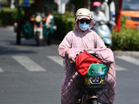 Citizens are wearing sun-protective clothing and riding on a street under high temperatures in Fuyang, China, on June 14, 2024. (