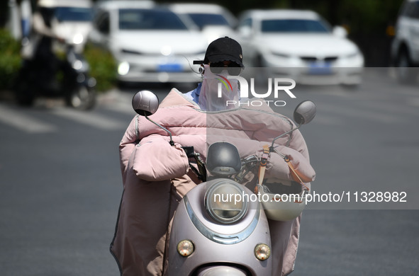 Citizens are wearing sun-protective clothing and riding on a street under high temperatures in Fuyang, China, on June 14, 2024. 