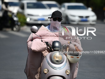 Citizens are wearing sun-protective clothing and riding on a street under high temperatures in Fuyang, China, on June 14, 2024. (