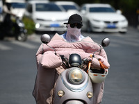 Citizens are wearing sun-protective clothing and riding on a street under high temperatures in Fuyang, China, on June 14, 2024. (