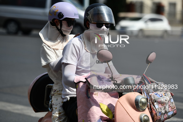 Citizens are wearing sun-protective clothing and riding on a street under high temperatures in Fuyang, China, on June 14, 2024. 