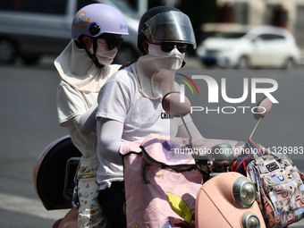 Citizens are wearing sun-protective clothing and riding on a street under high temperatures in Fuyang, China, on June 14, 2024. (