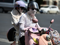 Citizens are wearing sun-protective clothing and riding on a street under high temperatures in Fuyang, China, on June 14, 2024. (