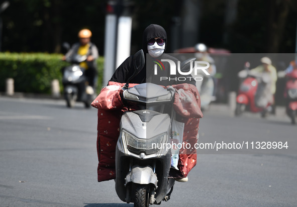 Citizens are wearing sun-protective clothing and riding on a street under high temperatures in Fuyang, China, on June 14, 2024. 