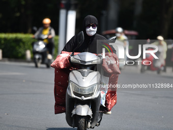 Citizens are wearing sun-protective clothing and riding on a street under high temperatures in Fuyang, China, on June 14, 2024. (