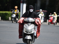 Citizens are wearing sun-protective clothing and riding on a street under high temperatures in Fuyang, China, on June 14, 2024. (