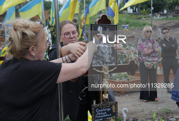 Women are attaching a photograph to a graveside cross during the funeral of Ukrainian serviceman, artist, musician, stylist, and queer commu...