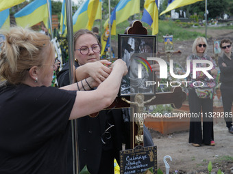 Women are attaching a photograph to a graveside cross during the funeral of Ukrainian serviceman, artist, musician, stylist, and queer commu...