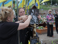 Women are attaching a photograph to a graveside cross during the funeral of Ukrainian serviceman, artist, musician, stylist, and queer commu...