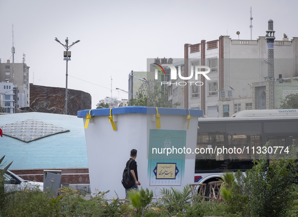 A young Iranian man is walking past a model of a ballot box that is being placed street-side in downtown Tehran, Iran, on June 14, 2024, dur...