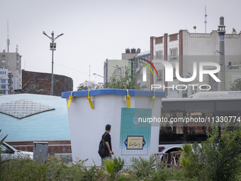 A young Iranian man is walking past a model of a ballot box that is being placed street-side in downtown Tehran, Iran, on June 14, 2024, dur...