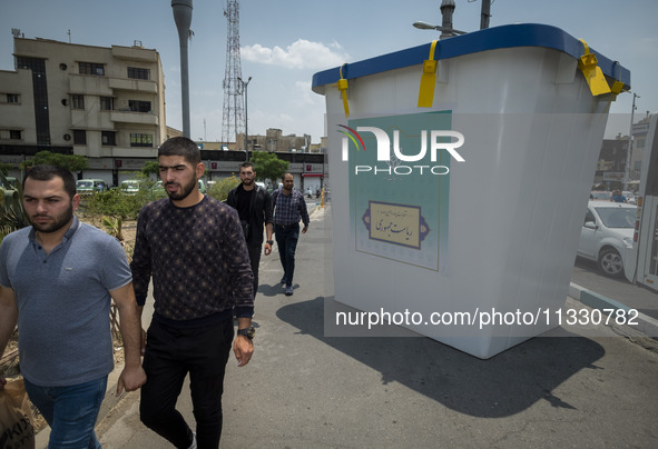 Iranian men are walking past a model of a ballot box that is being placed street-side in downtown Tehran, Iran, on June 14, 2024, during Ira...