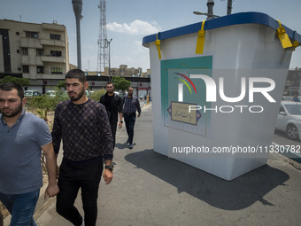 Iranian men are walking past a model of a ballot box that is being placed street-side in downtown Tehran, Iran, on June 14, 2024, during Ira...